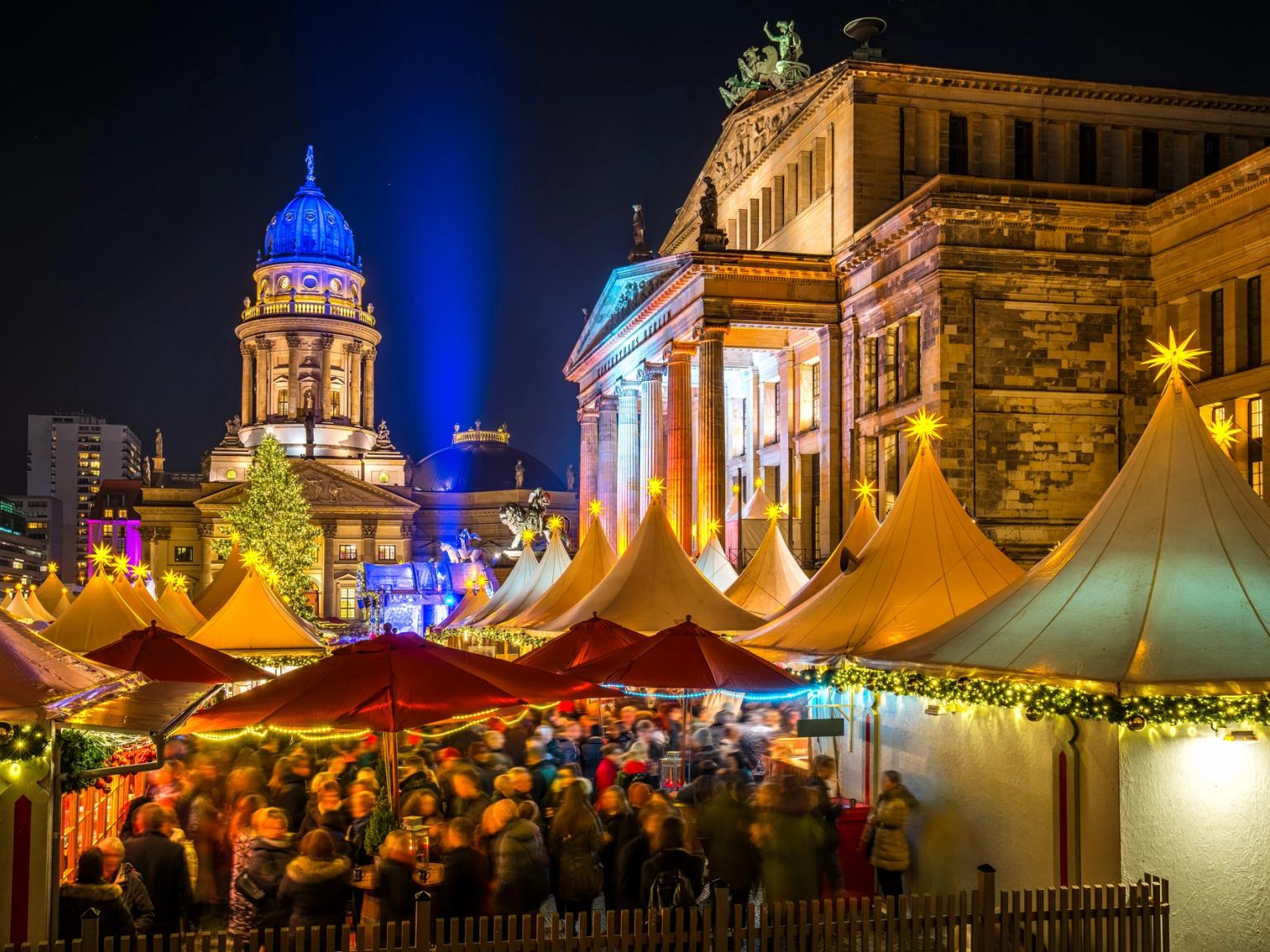 Et travelt julemarked om natten med opplyste boder, folkemengder og historiske bygninger i bakgrunnen i Berlin.
