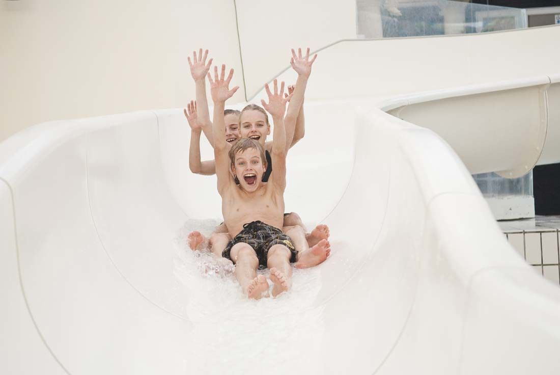 Tre uppspelta barn åker nerför en vattenrutschkana med armarna uppsträckta.