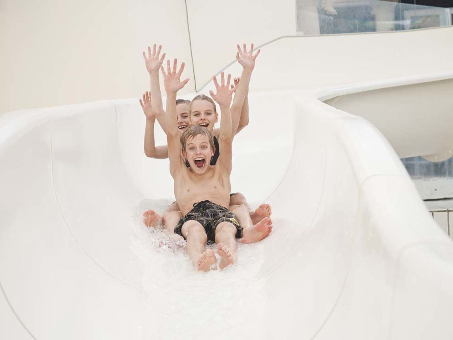 Tre uppspelta barn åker nerför en vattenrutschkana med armarna uppsträckta.