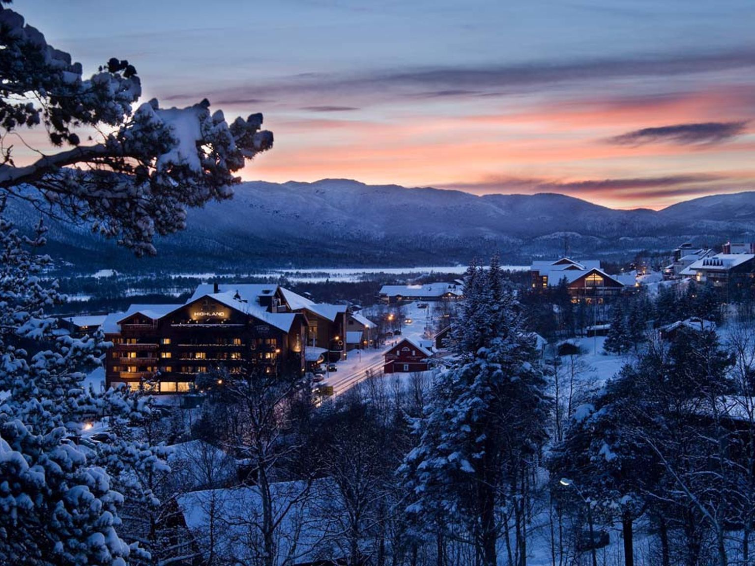 et snødekt skianlegg ved solnedgang med fjell i bakgrunnen