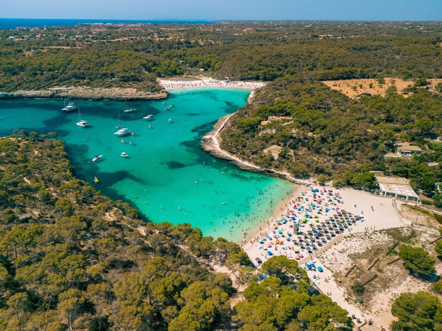 Flygvy över en turkos bukt med livliga stränder, båtar och gröna skogar. Mallorca, Spanien