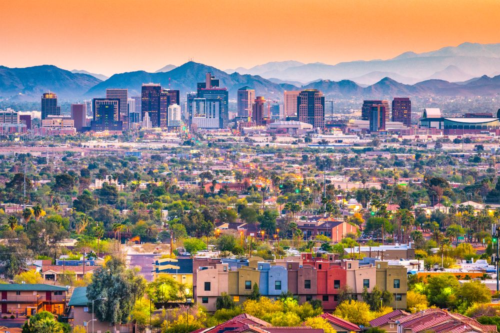 Panoramisk udsigt over en bysilhuet, boligområder og bjerge ved solnedgang. Phoenix, Arizona