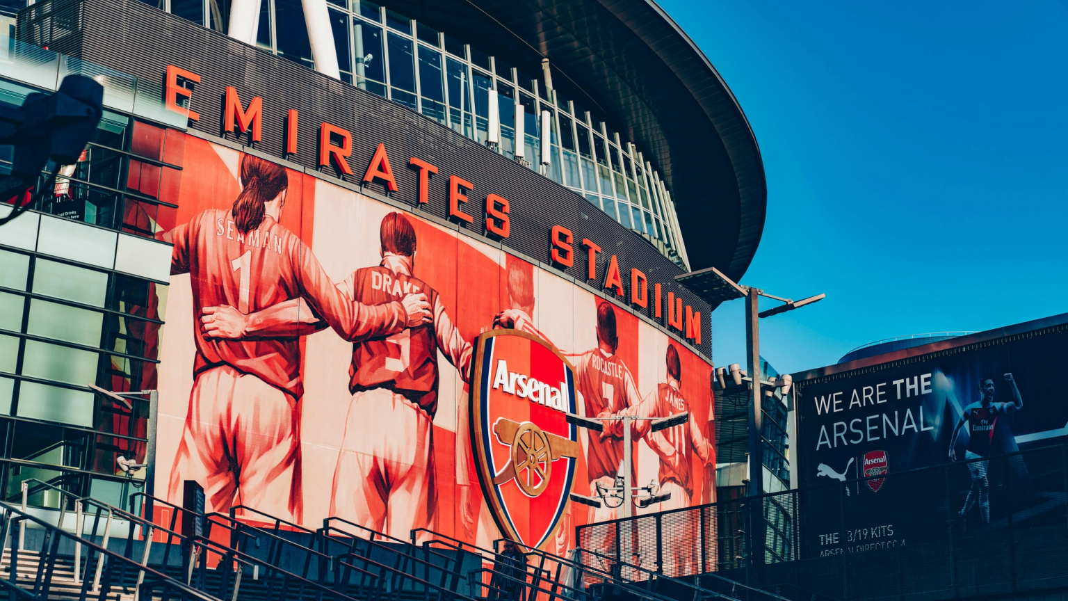 Exterior of Emirates Stadium with a large mural of Arsenal players and the club crest.
