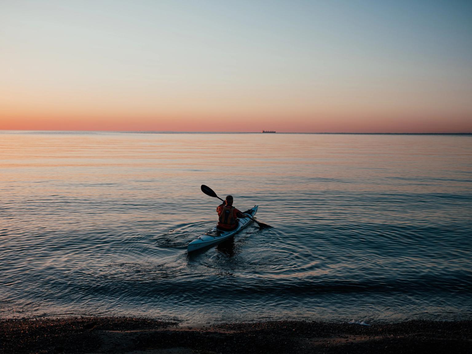 en man paddlar en kajak i havet vid solnedgången