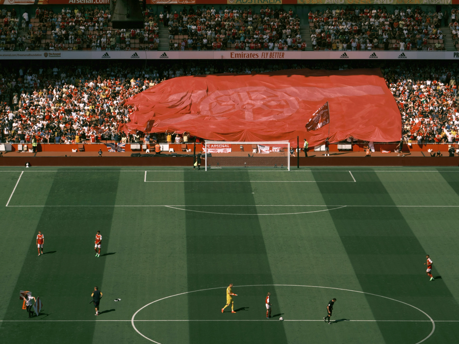 An elevated view of a football stadium with players on the pitch and a massive red banner covering the stands.