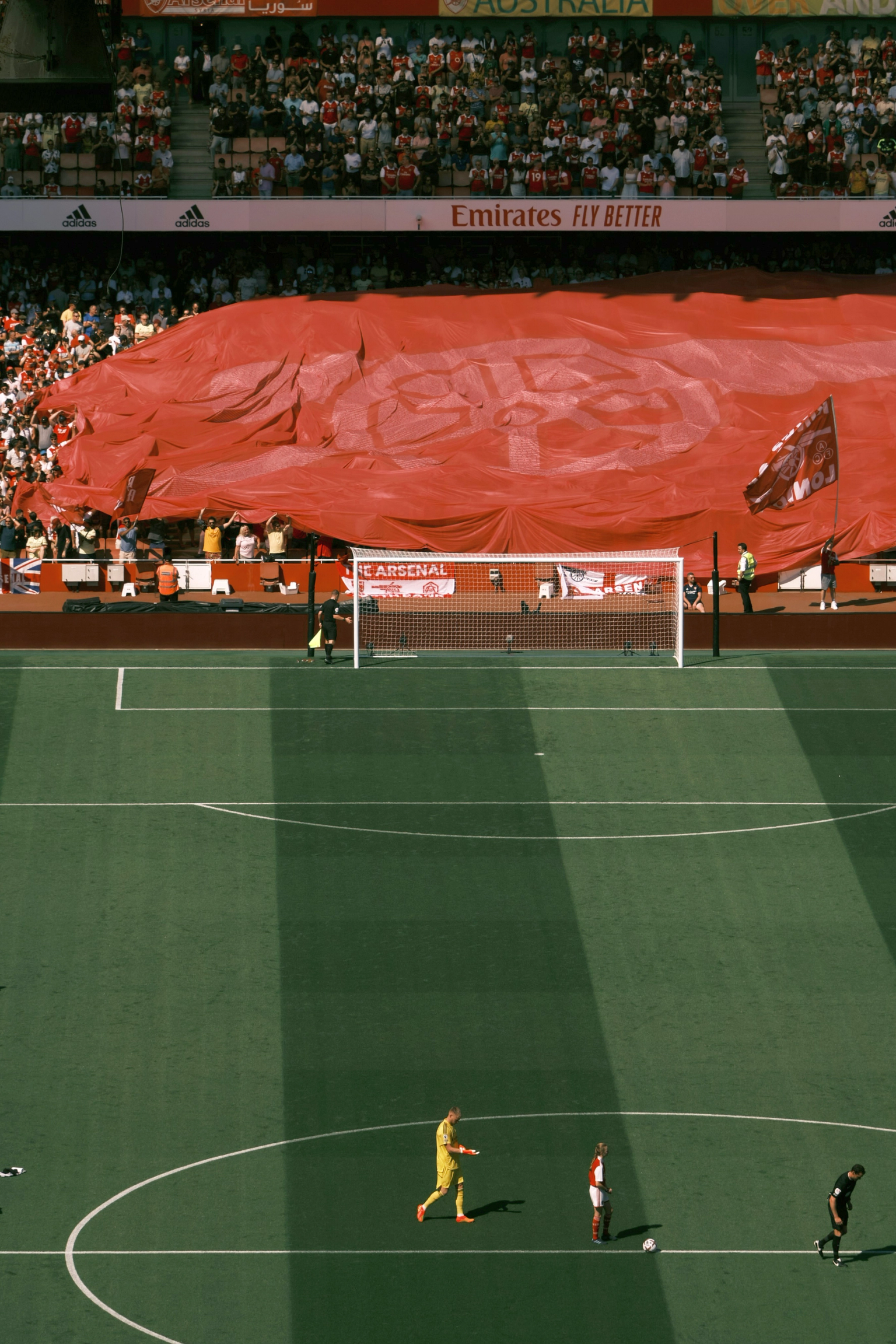 An elevated view of a football stadium with players on the pitch and a massive red banner covering the stands.