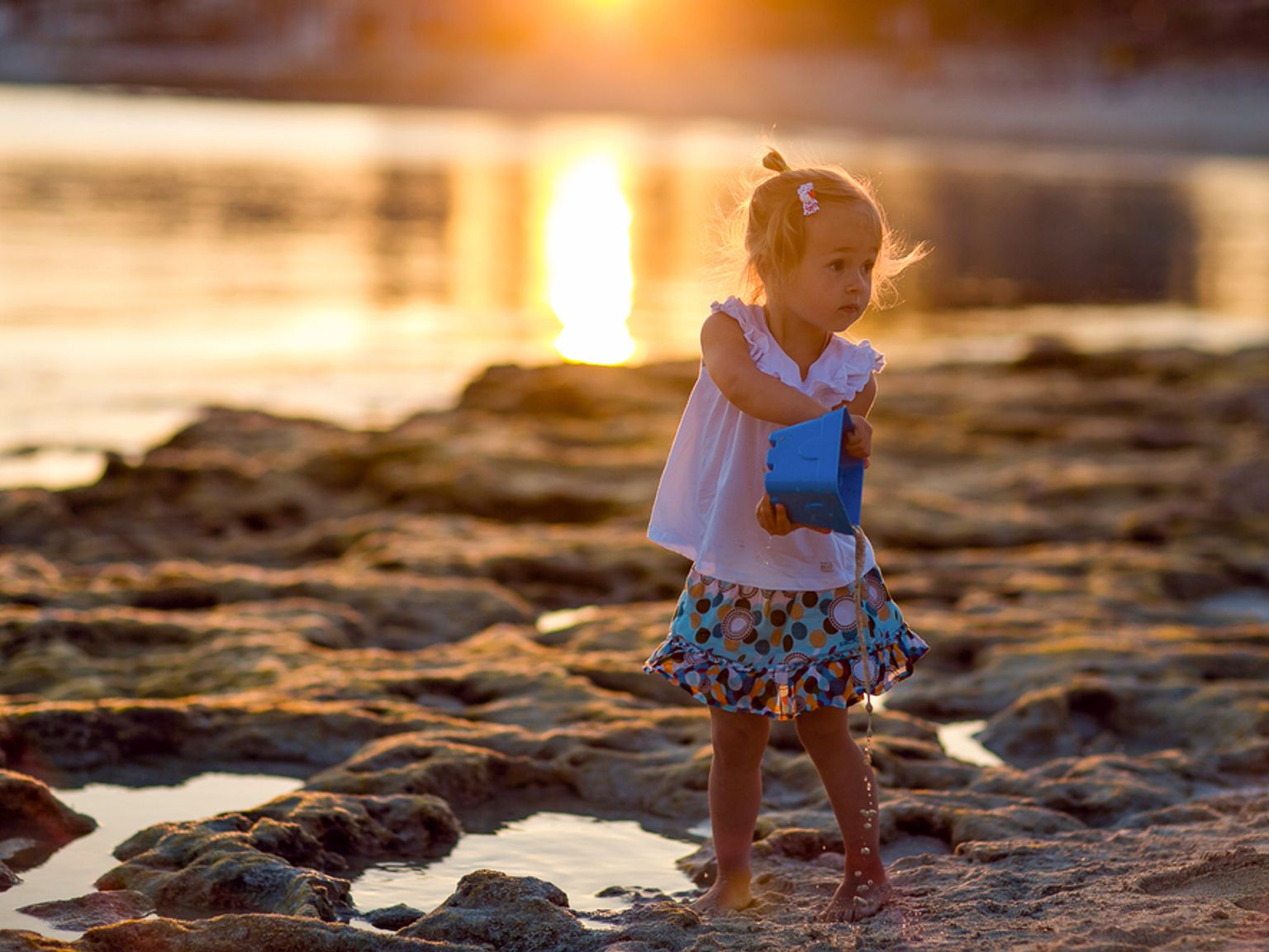 en liten jente leker på stranden ved solnedgang