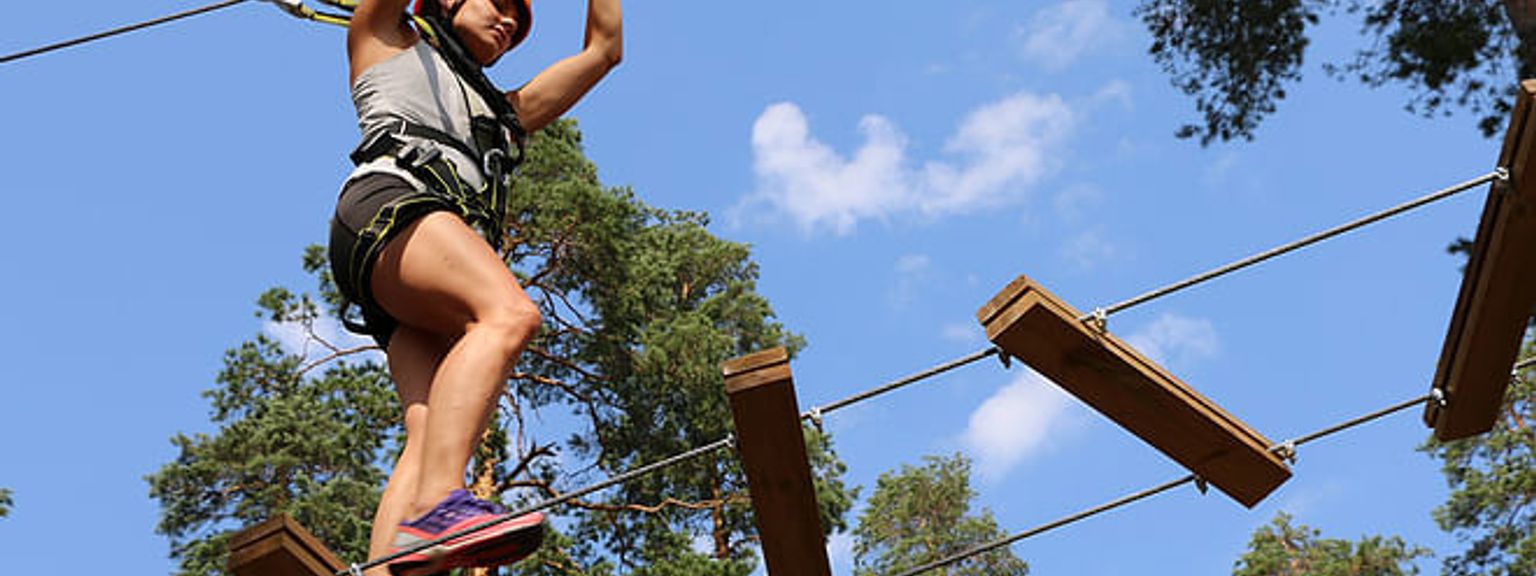 a woman is standing on a ropes course in the woods