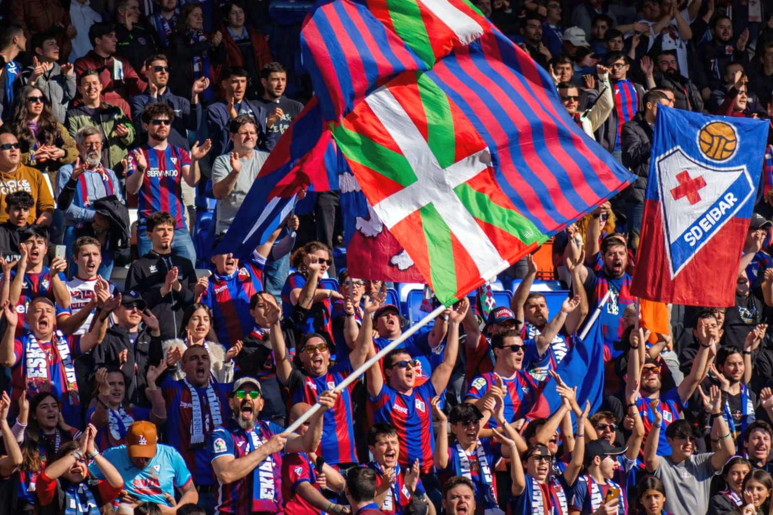 Football fans cheering and waving Basque and SD Eibar flags.