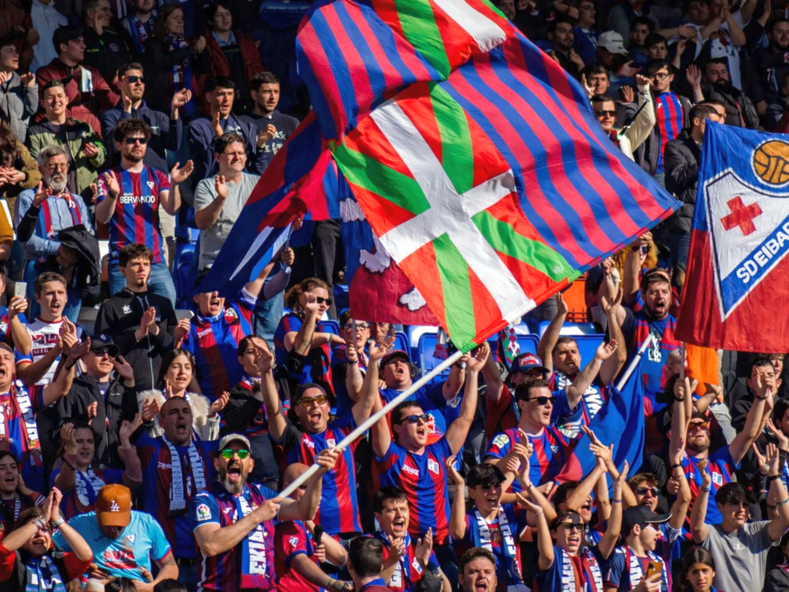 Football fans cheering and waving Basque and SD Eibar flags.