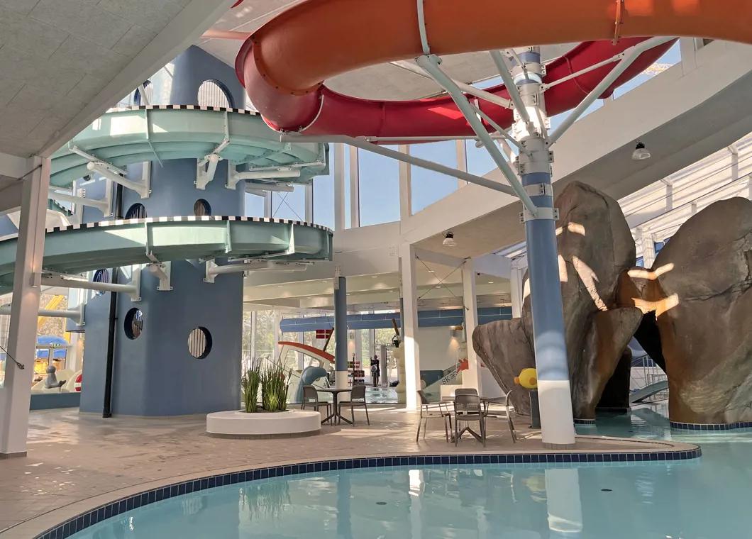 Inomhusvattenpark med ett blått rutschkanetorn, röd och orange tubrutschbana, simbassäng och klippfunktioner.