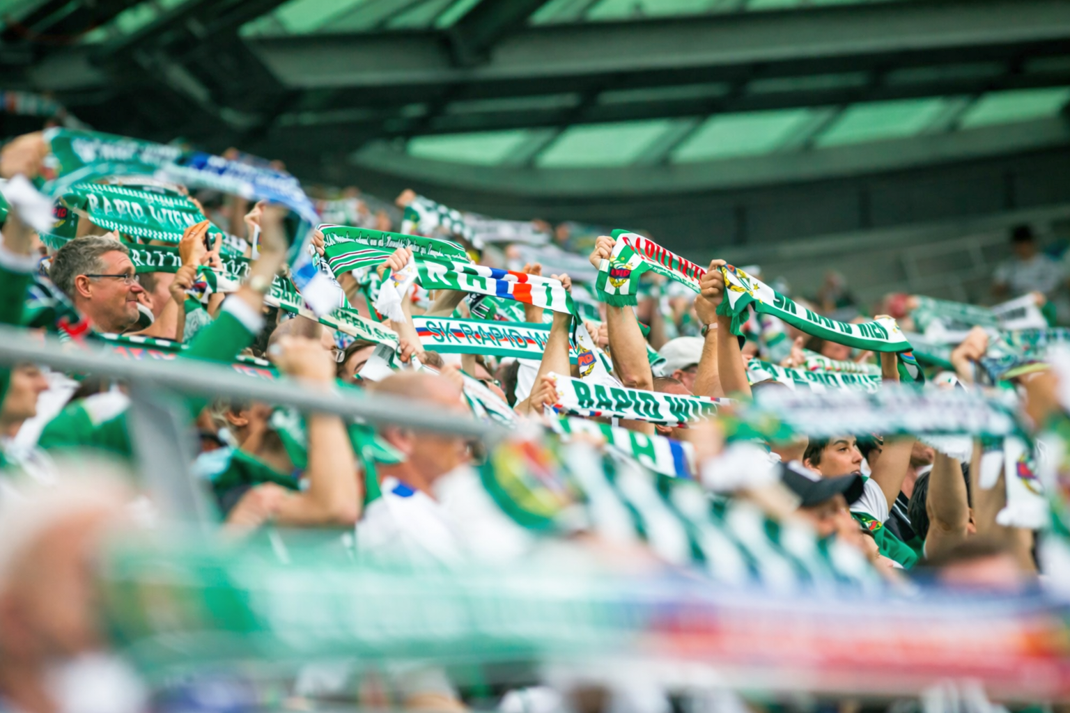Fans halten grüne und weiße Schals im Stadion hoch.