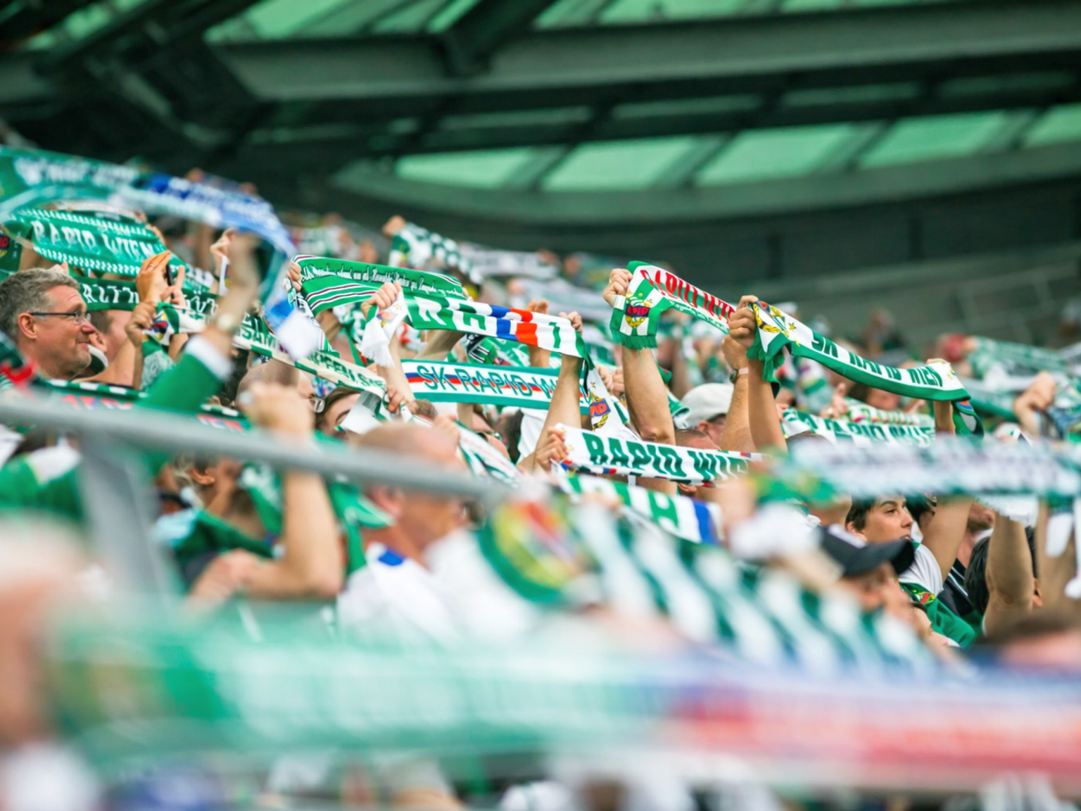 Fans halten grüne und weiße Schals im Stadion hoch.
