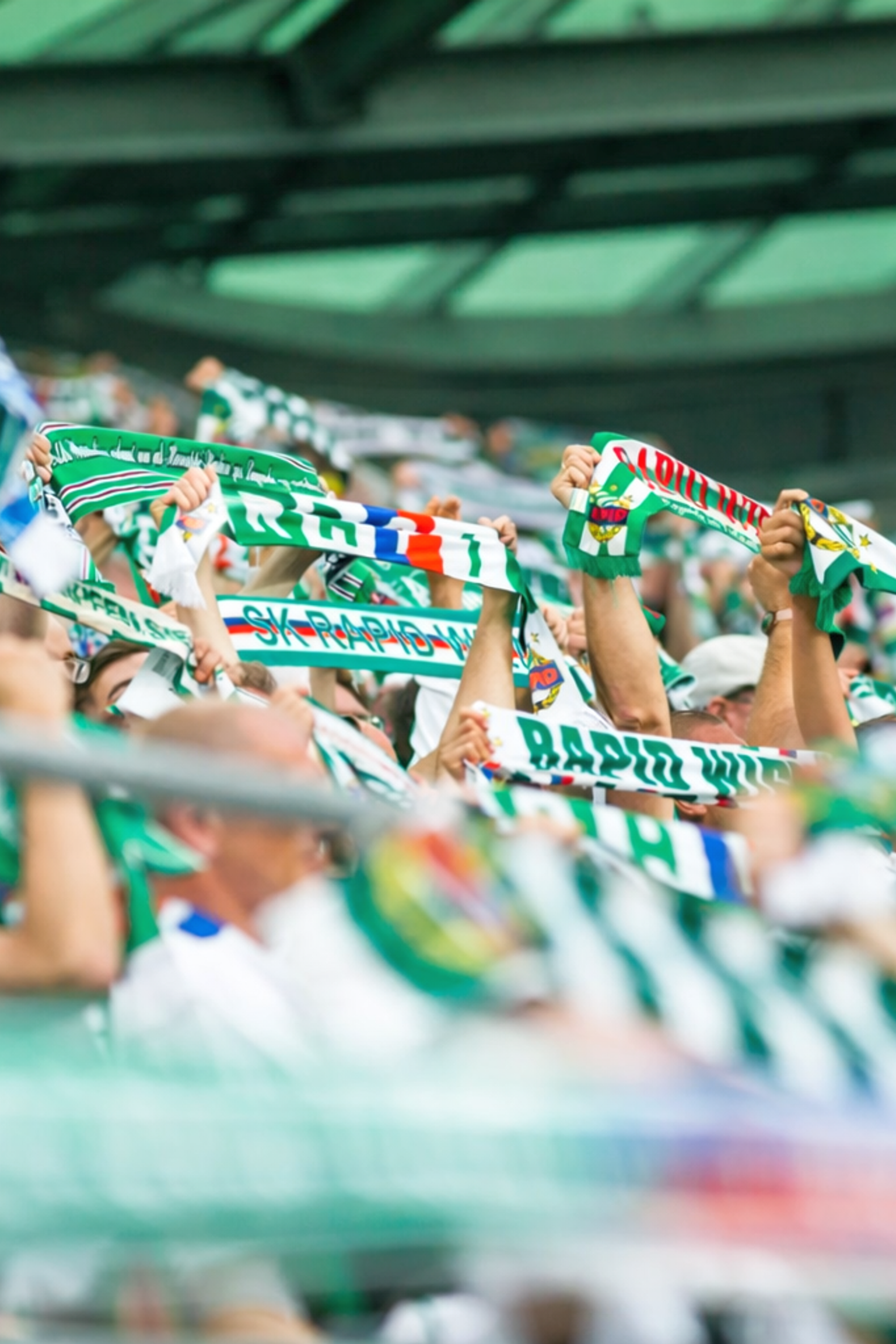 Fans halten grüne und weiße Schals im Stadion hoch.