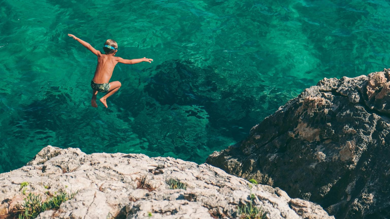 un jeune garçon saute dans l'océan depuis une falaise