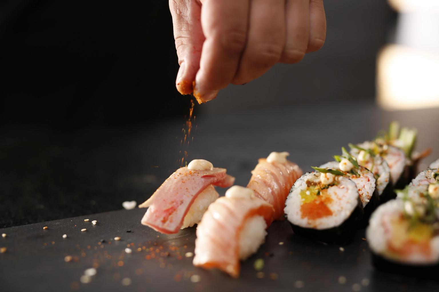 a person is adding spices to a tray of sushi
