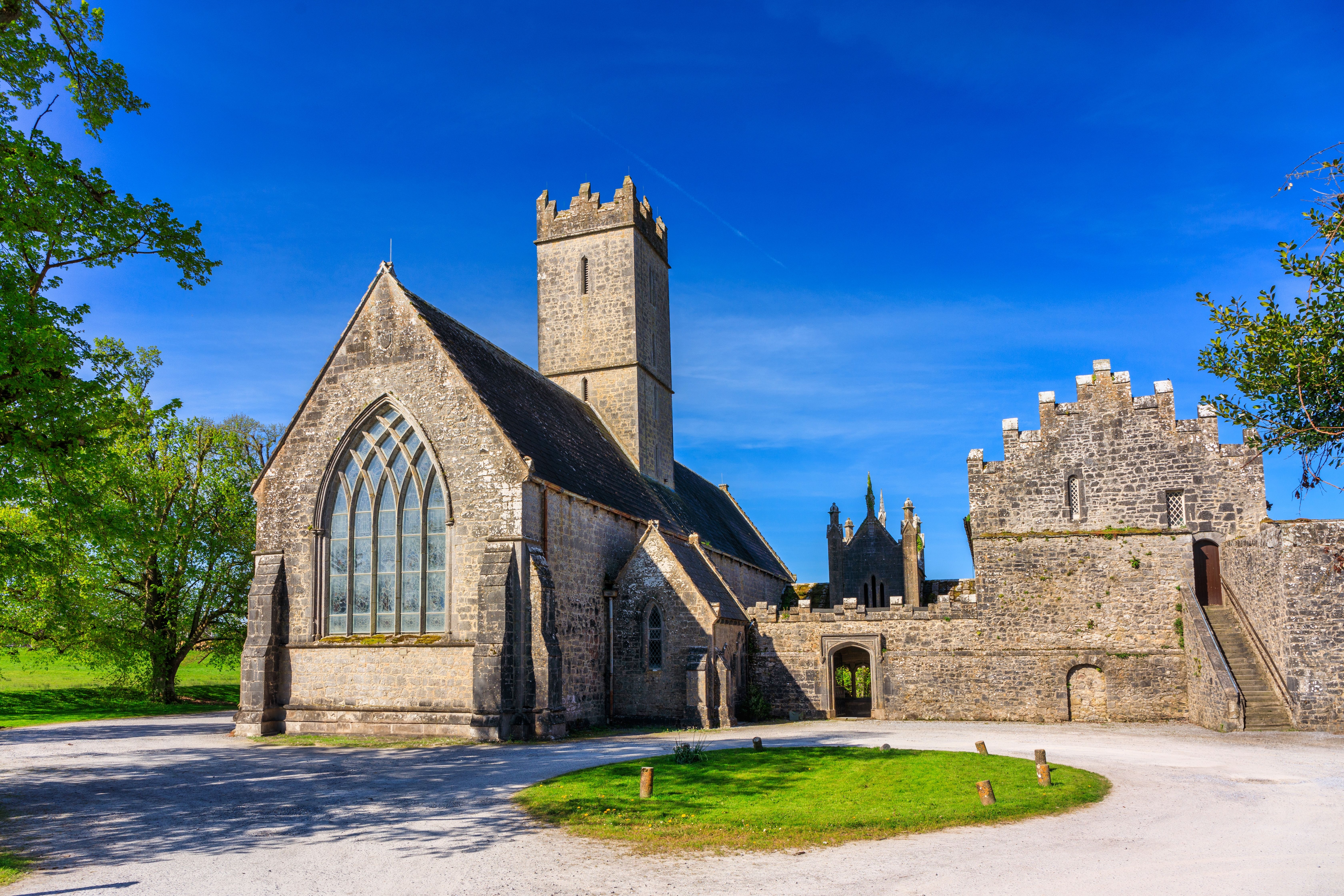 Stone abbey ruins with a tall tower and large arched window against a blue sky.