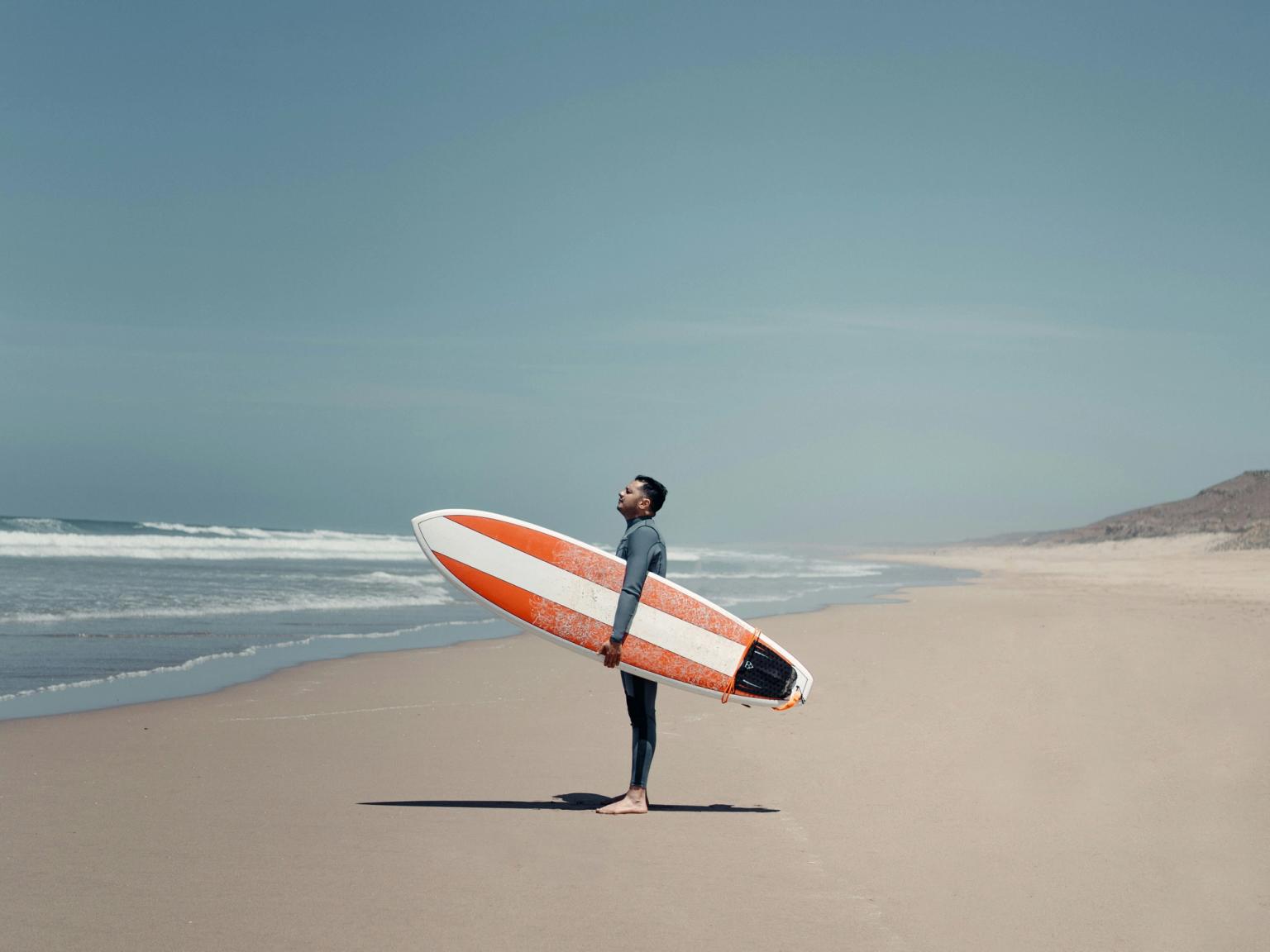 a man standing on a beach holding a surfboard