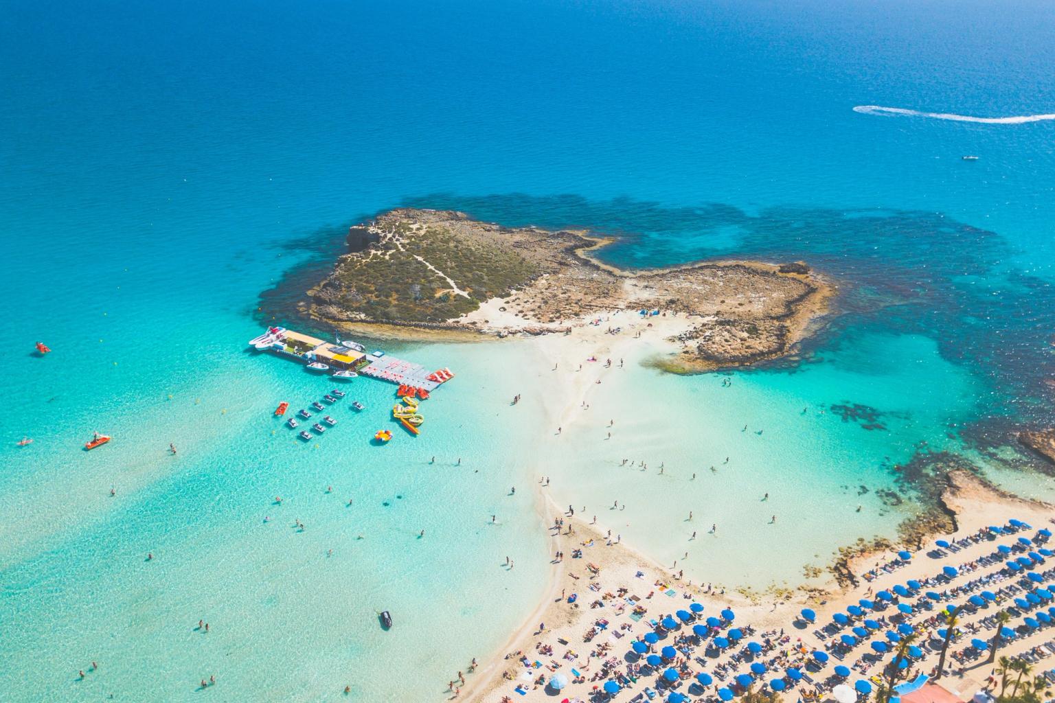 en flygvy över en tropisk strand fylld med människor och paraplyer
