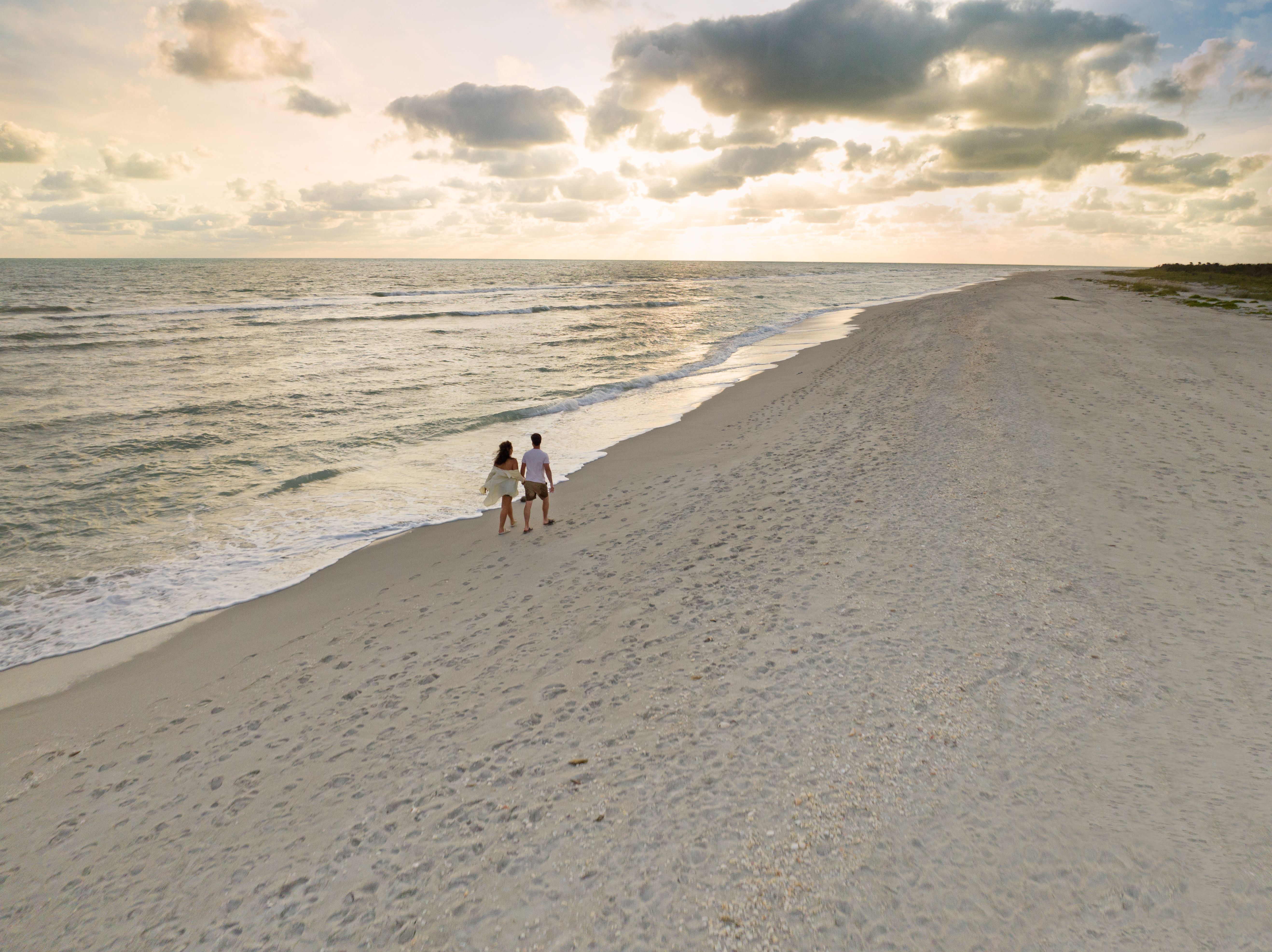 et luftfoto av et par som går på en strand ved solnedgang