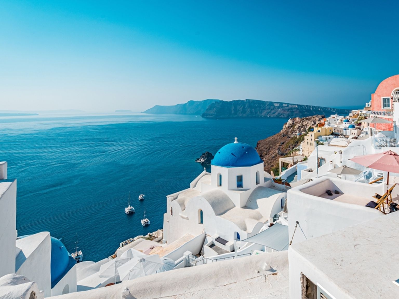 Hvite bygninger med blå kupler i Santorini med utsikt over det dypblå havet. Santorini, Hellas