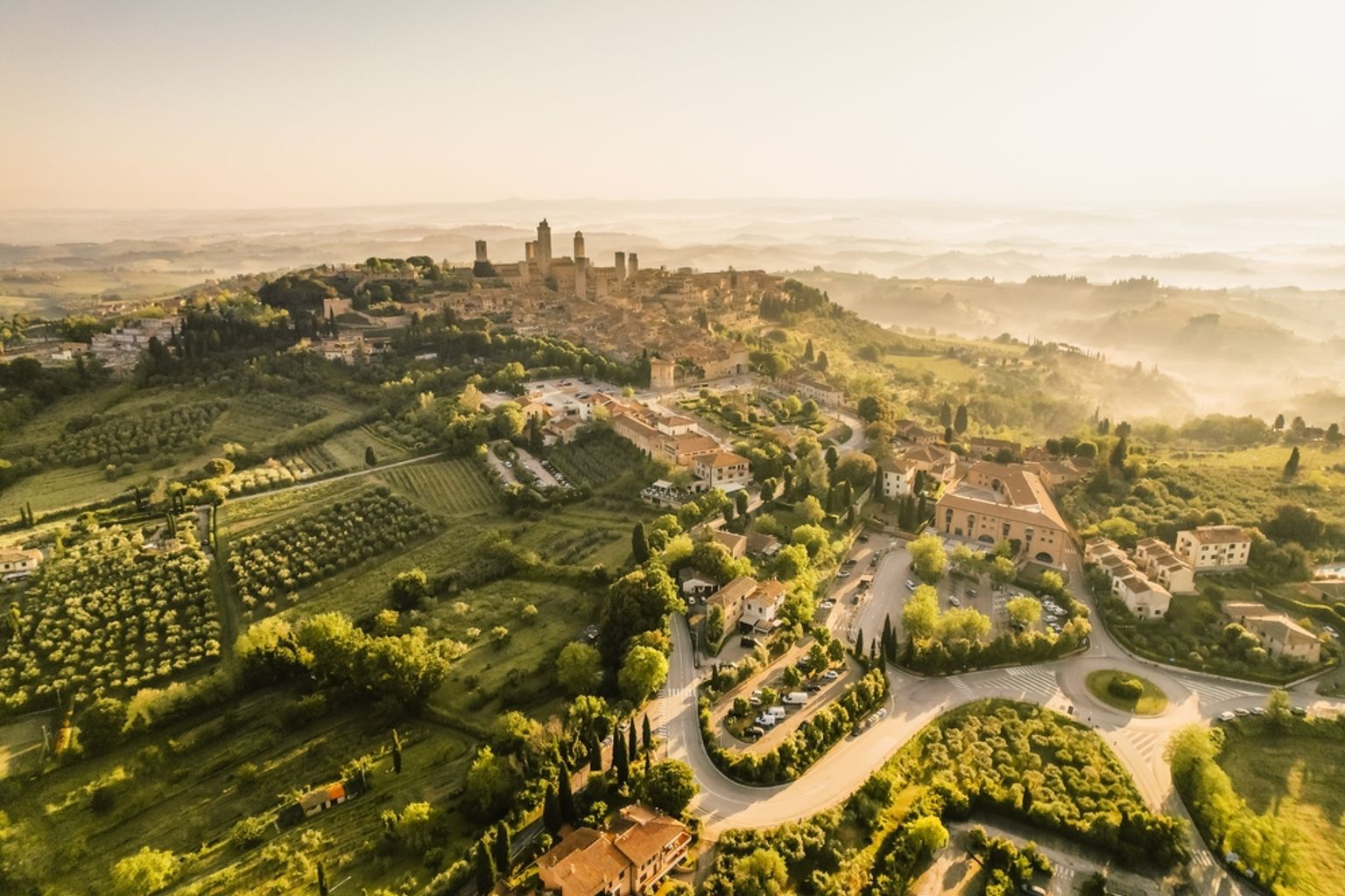 et luftfoto af en lille by på toppen af en bakke omgivet af træer og marker