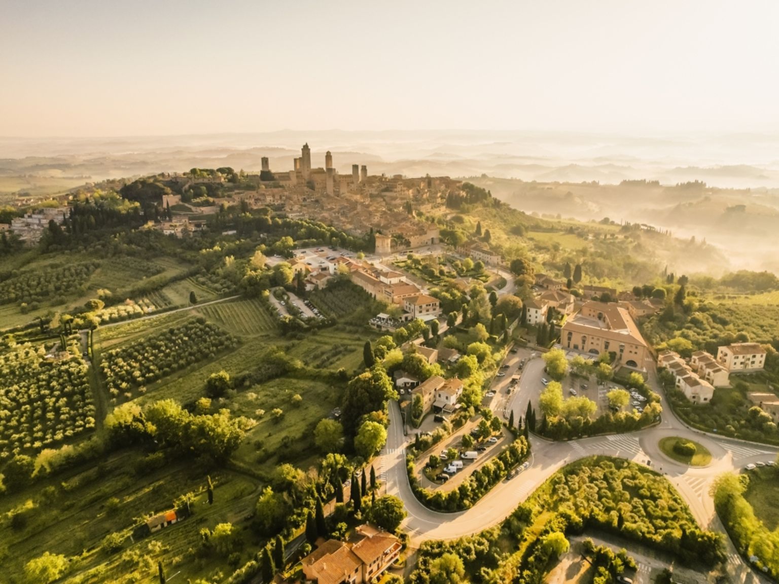 en flygvy av en liten stad på toppen av en kulle omgiven av träd och fält