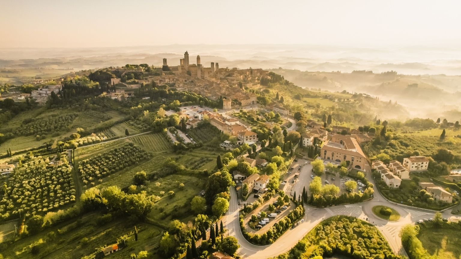 et luftfoto af en lille by på toppen af en bakke omgivet af træer og marker