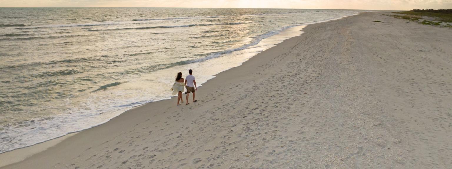 en flygvy av ett par som går på en strand vid solnedgången.