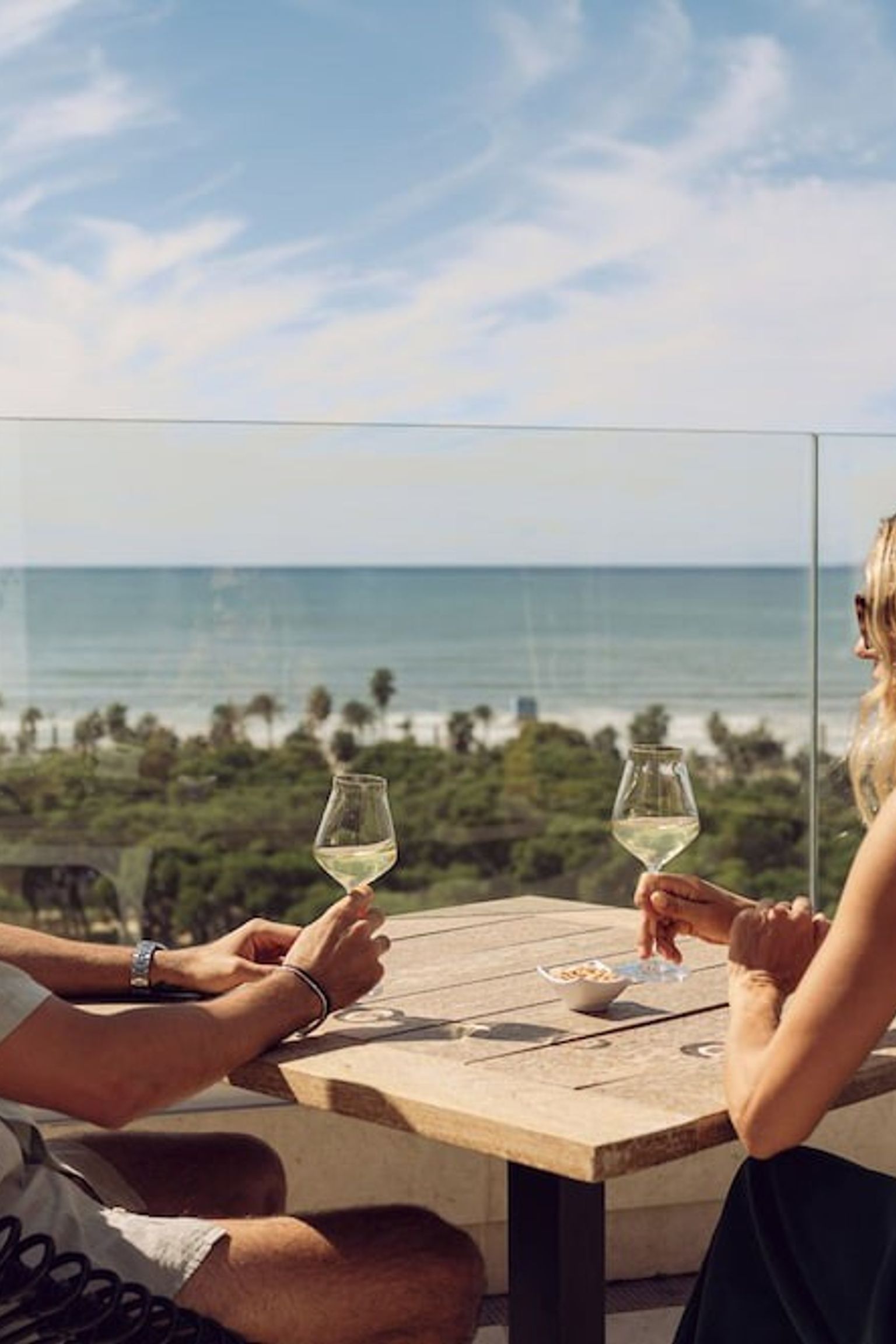 Zwei Personen trinken Weißwein auf einem sonnigen Balkon mit Blick auf Meer und Stadt. Iberostar Selection Llaut Palma – Nur für Erwachsene