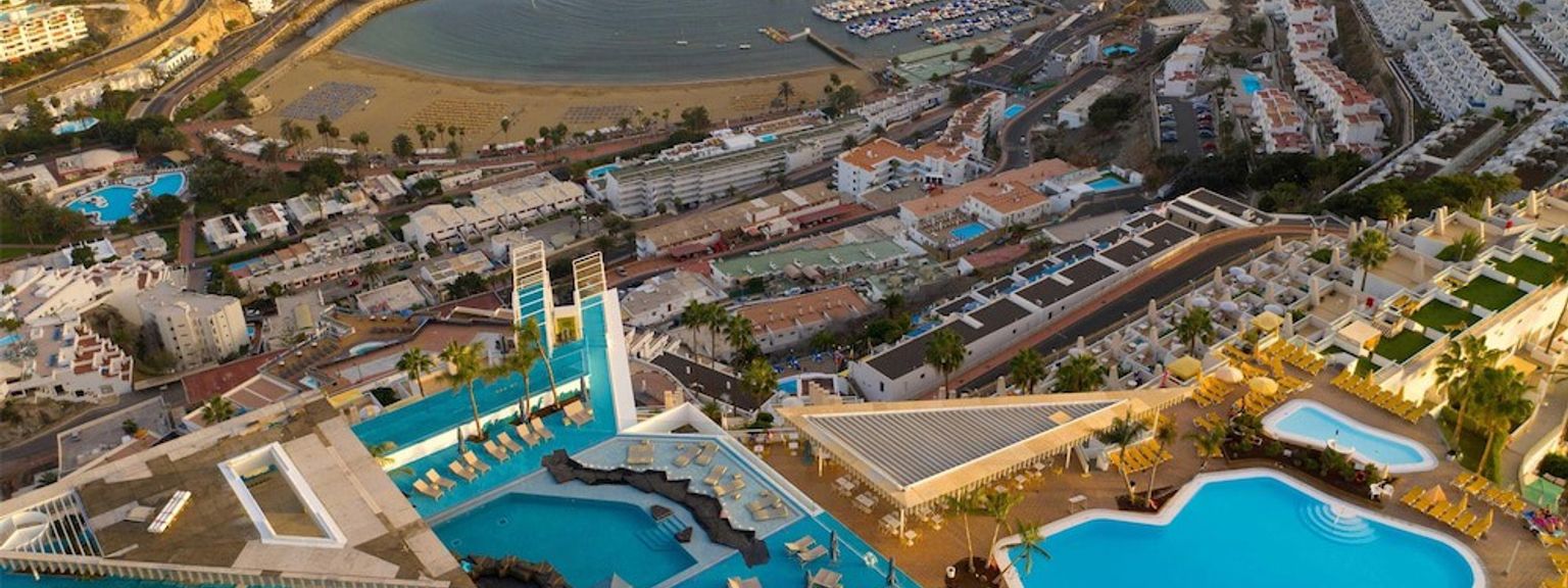 Flygfoto av en kustort med flera swimmingpooler, en marina och en strand.