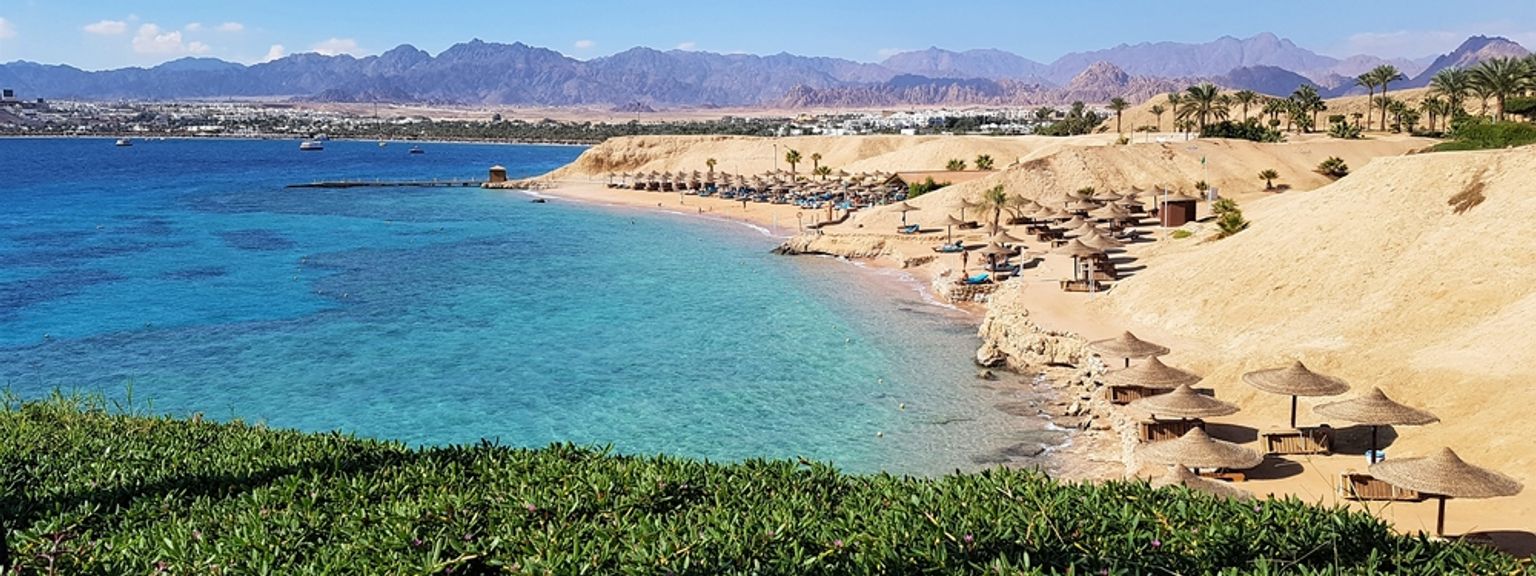 ein Strand mit Sonnenschirmen und Stühlen darauf und Bergen im Hintergrund