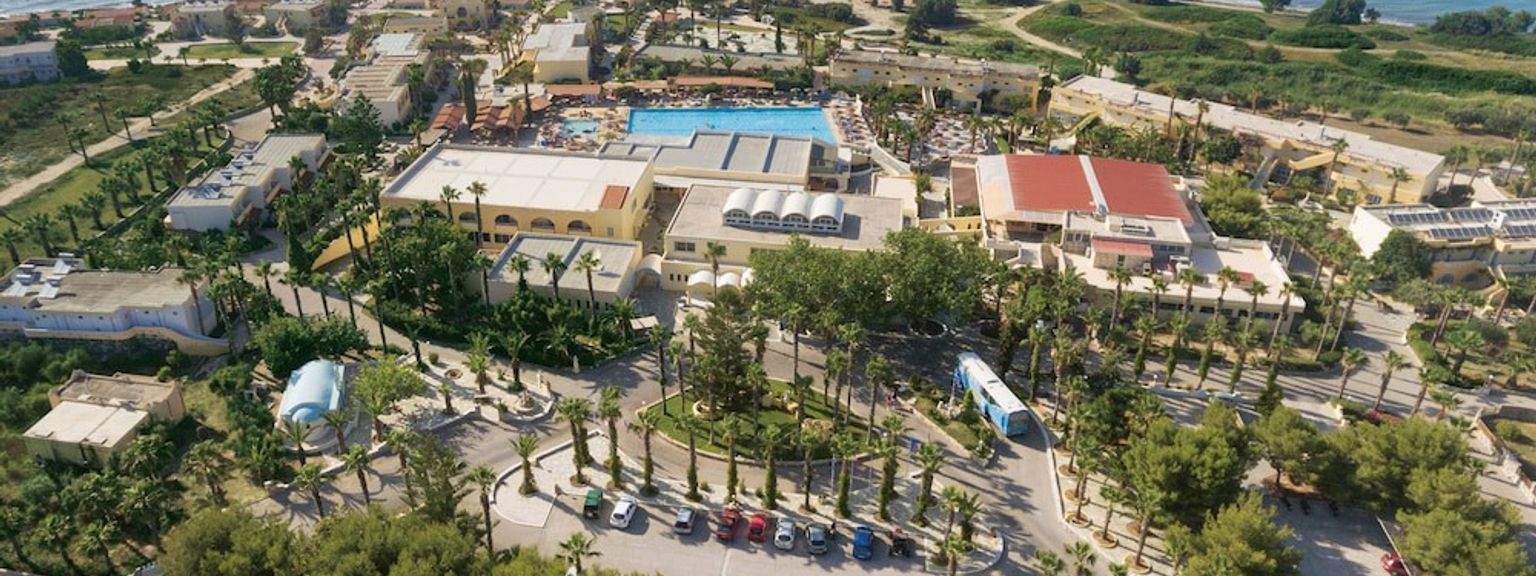 et luftfoto af et stort feriested omgivet af træer og palmer ved siden af havet