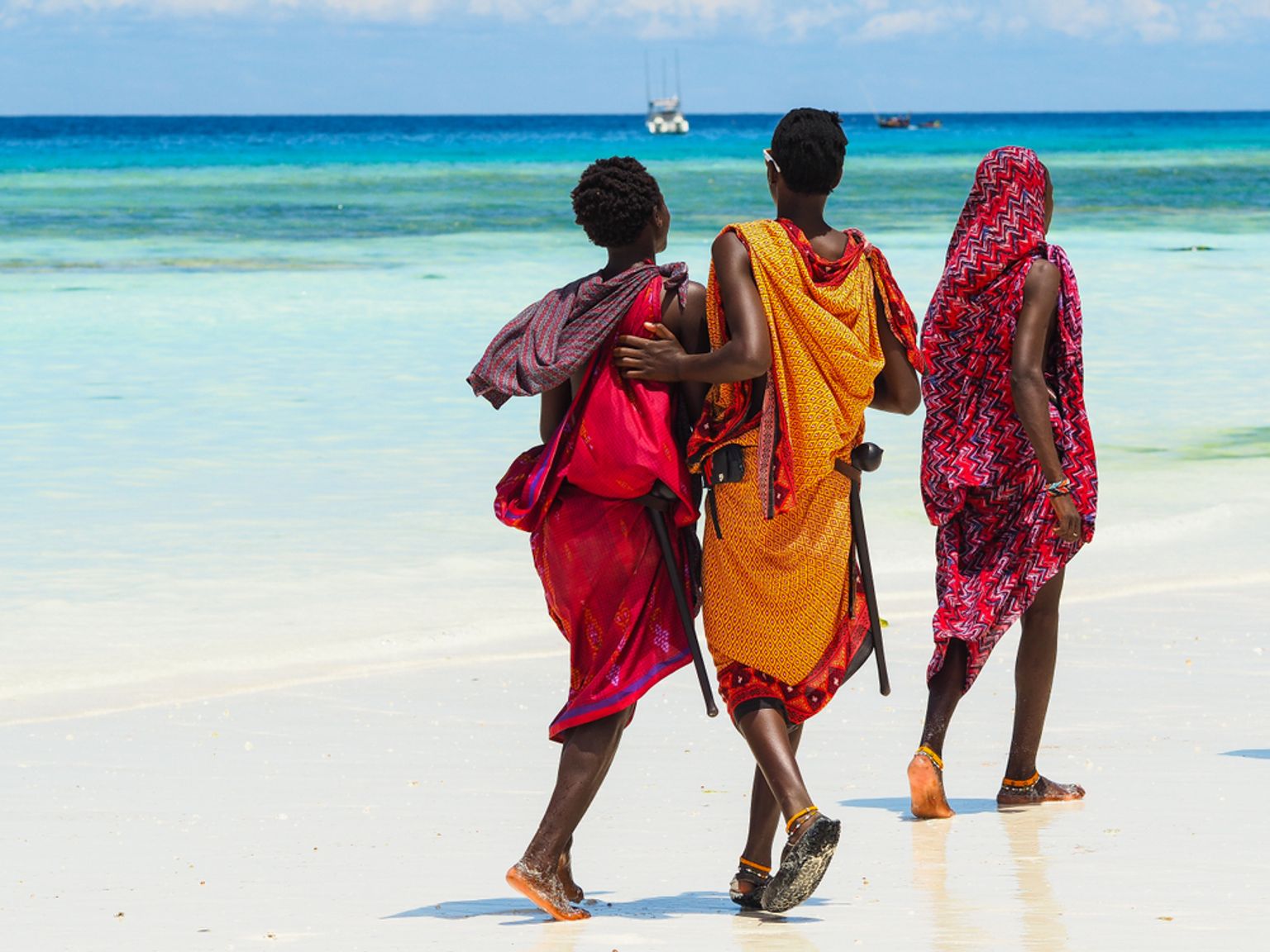 tre personer går på en strand med en båt i bakgrunden, Nungwi, Zanzibar