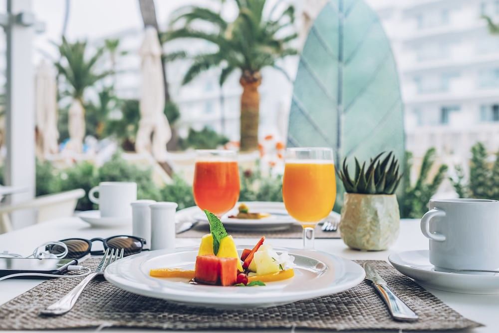 En tropisk frukostbuffé med frukt, juicer och kaffe på ett utomhusbord. Iberostar Waves Alcudia Park