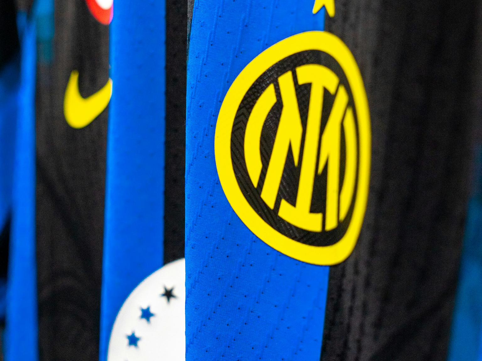Close-up of an Inter Milan football jersey showing the yellow club logo, star, Nike swoosh, and Italian flag badge on blue and black stripes.
