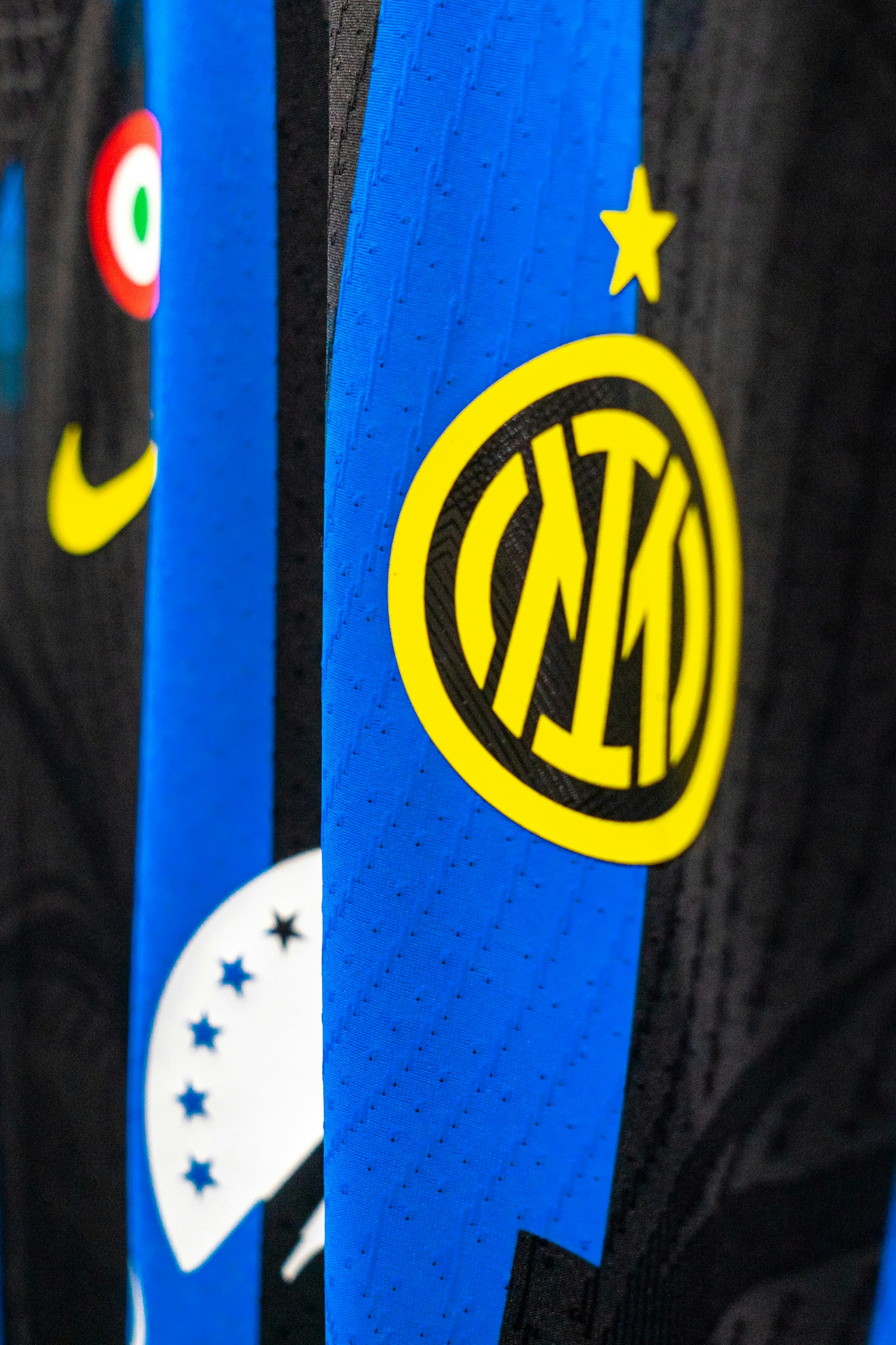 Lähikuva Inter Milan jalkapallopaidasta, jossa näkyy keltainen seuralogo, tähti, Nike swoosh ja Italian lipun merkki sinisillä ja mustilla raidoilla.