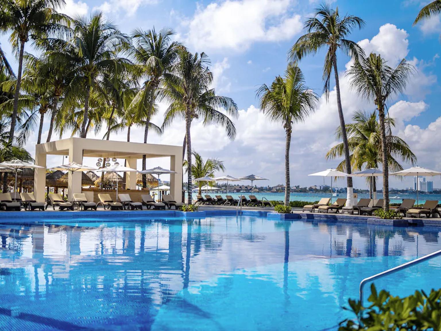 et stort svømmebasseng omgitt av palmetrær og stoler på et feriested