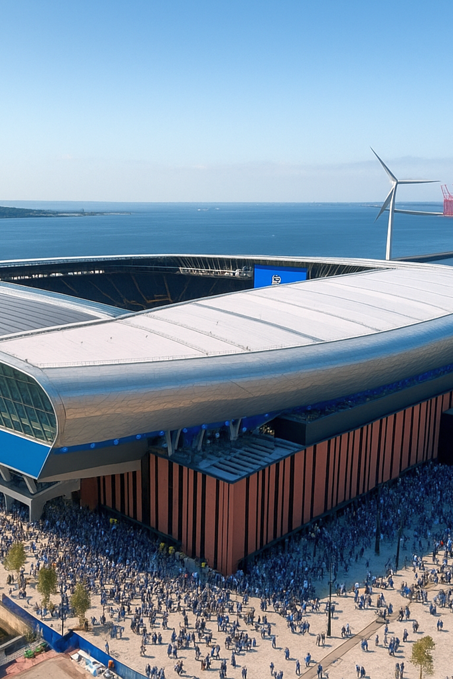 Vista aérea do moderno estádio Hill Dickinson, rodeado por multidões, próximo à água com turbinas eólicas e edifícios industriais ao fundo.