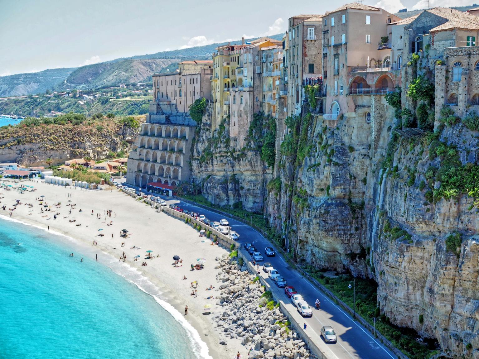 Edifici colorati su scogliere che si affacciano su una spiaggia sabbiosa e un mare turchese. Tropea, Calabria