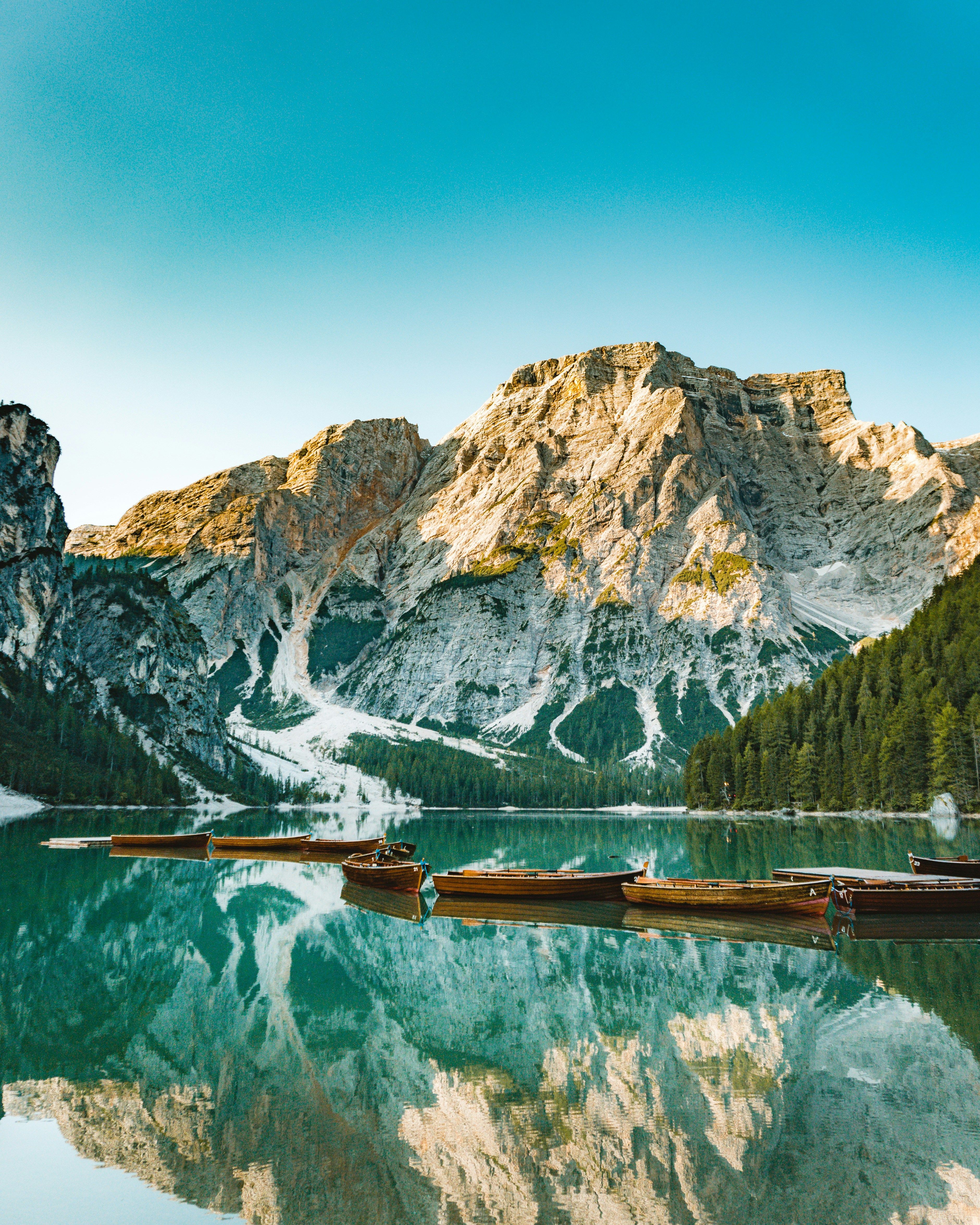 Tre båter på en smaragdgrønn fjellsjø som speiler røffe fjelltopper og en blå himmel. Lago di Braies, Italia