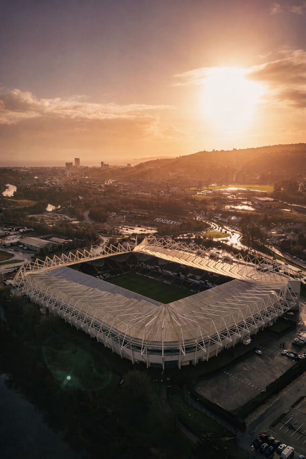 Aerial view of a stadium and city glowing under a golden sunset.