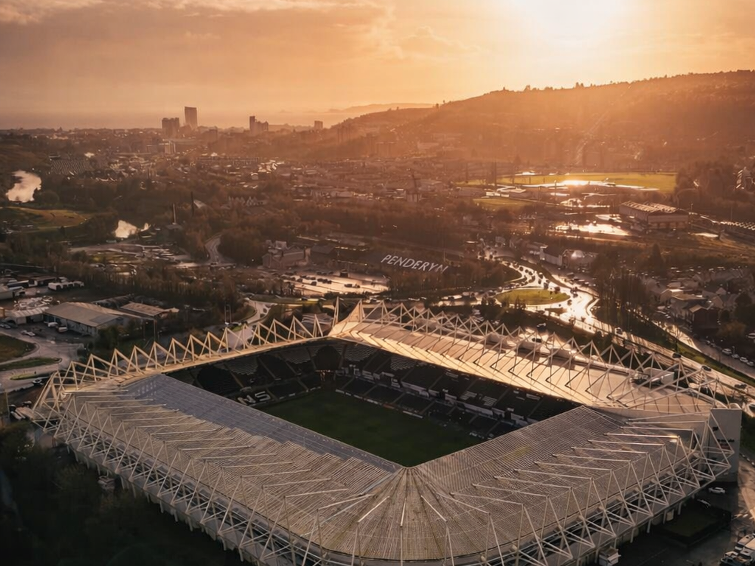 Aerial view of a stadium and city glowing under a golden sunset.