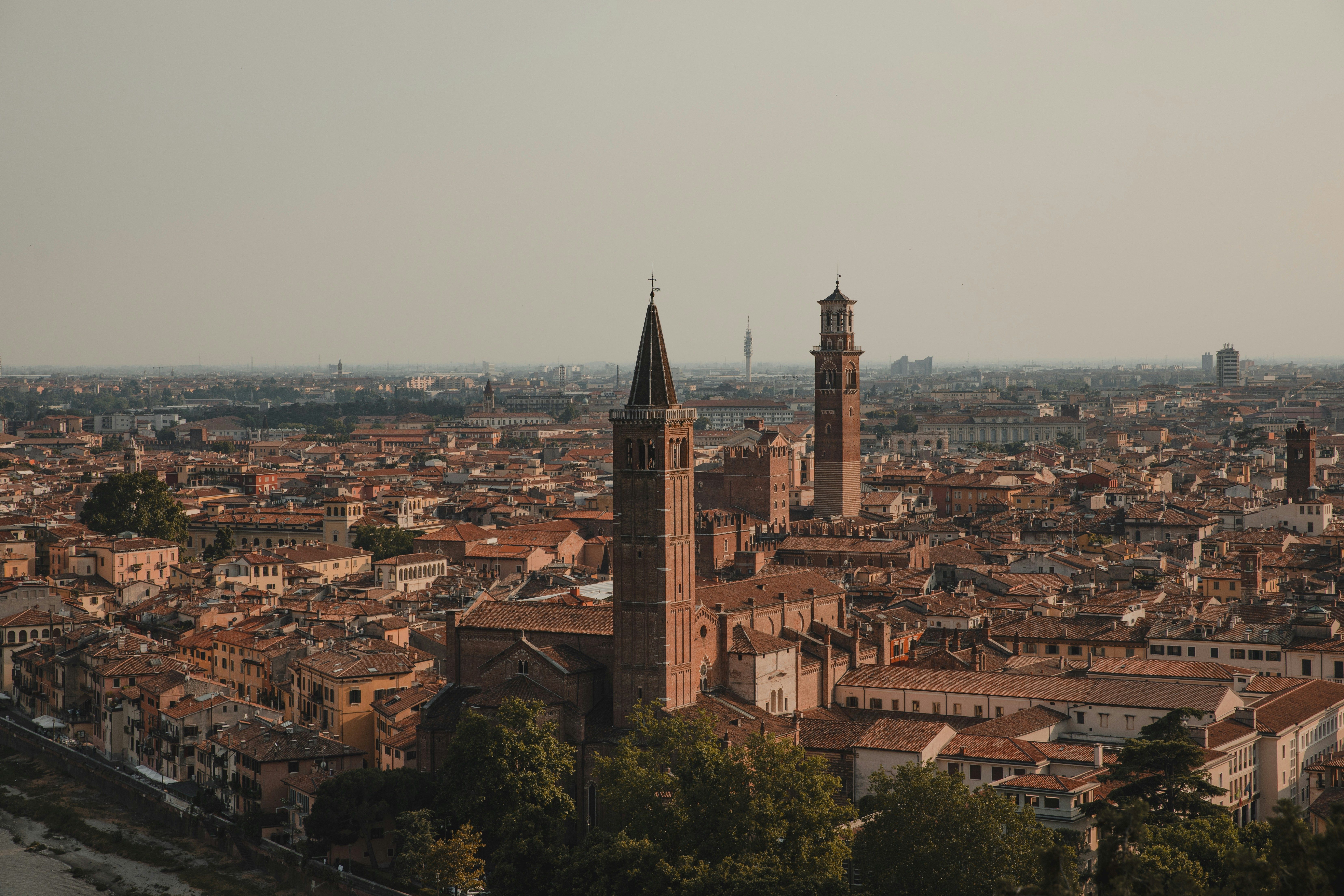 Veronas bysilhuett med rødtegltak og to fremtredende historiske tårn under en disig himmel.