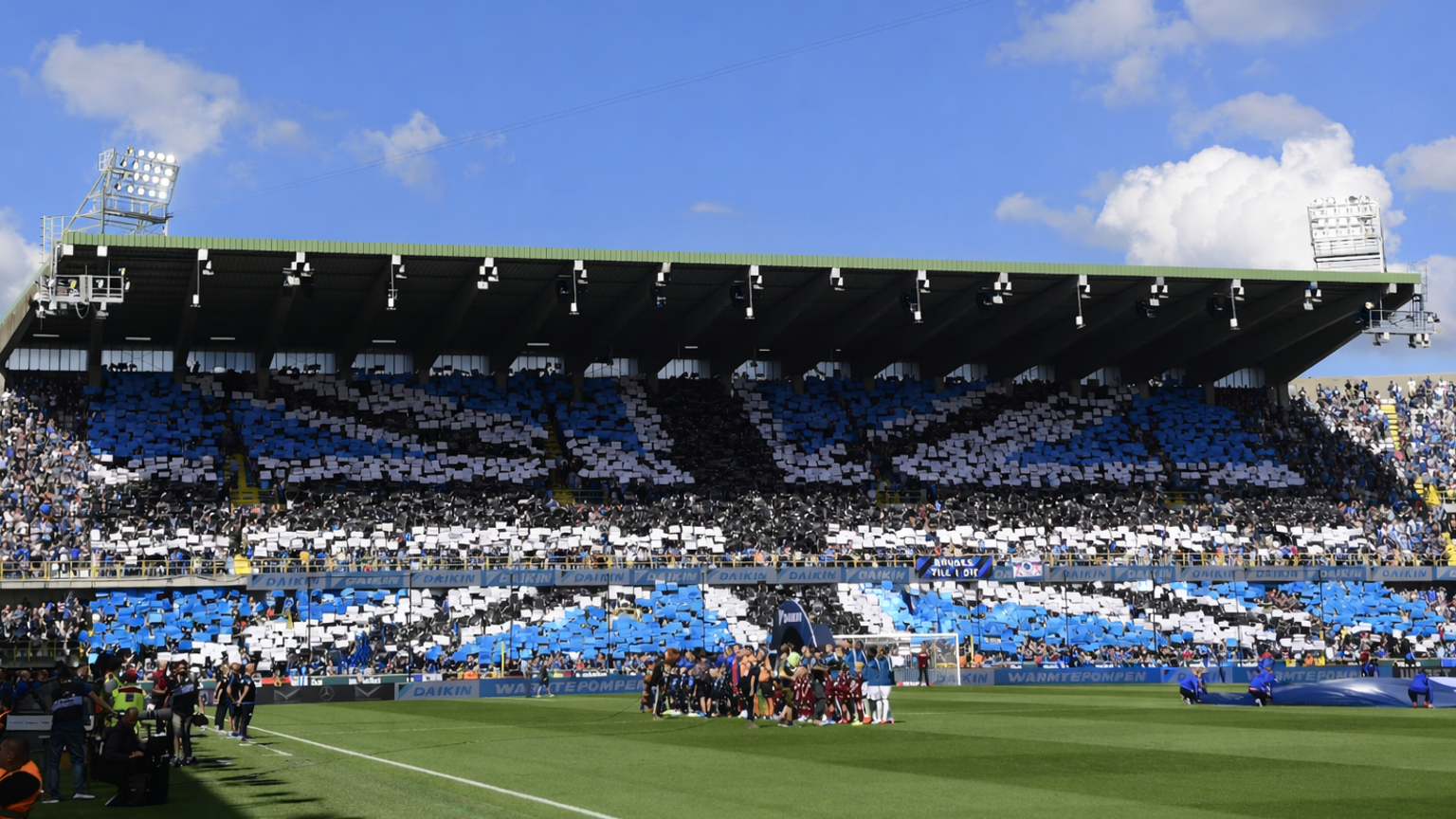 A soccer stadium full of fans displaying a blue, black, and white tifo spelling "ALE" in the stands.