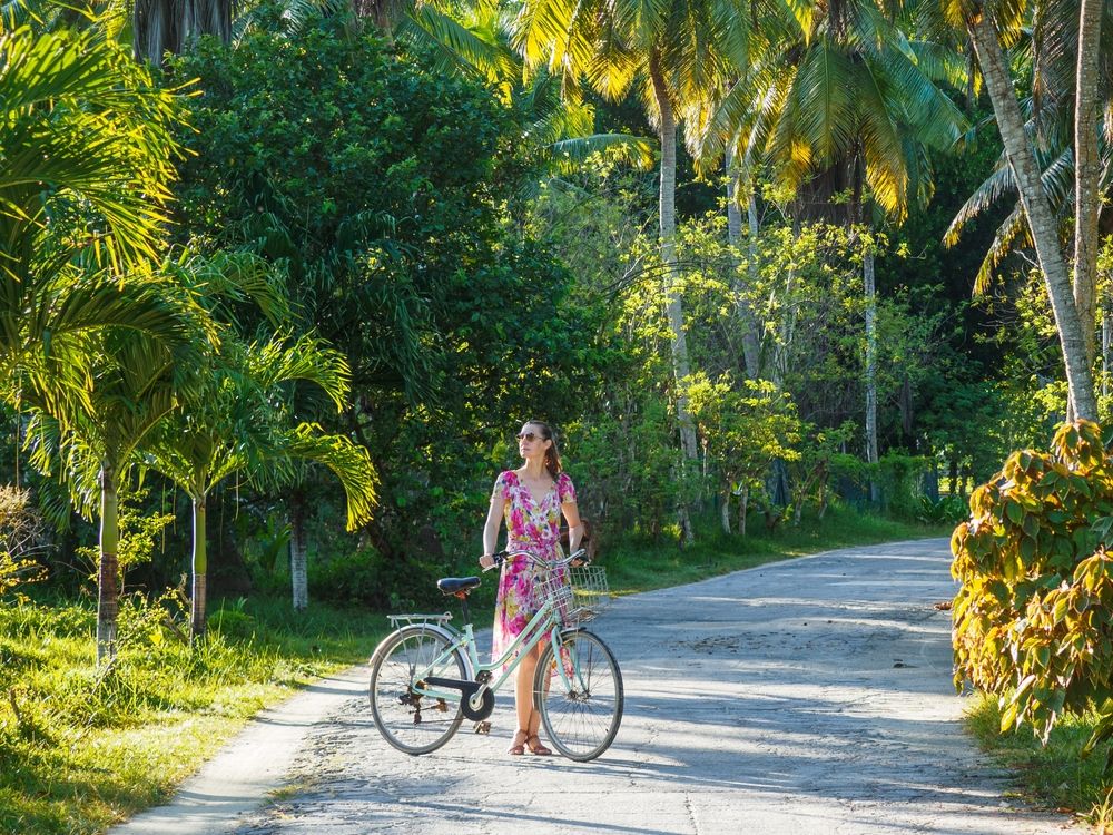 En kvinna i en blommig klänning leder en cykel på en solig tropisk väg. Seychellerna.