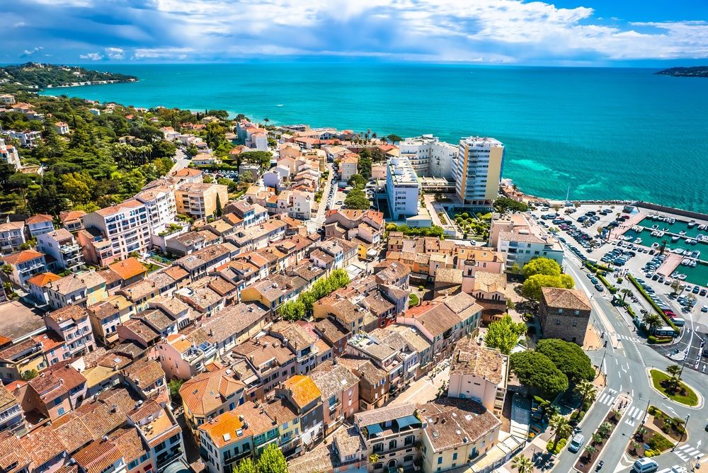 Luftfoto av en kystby med rød-takede bygninger, en marina og turkis hav under en blå himmel. Sainte-Maxime, Frankrike