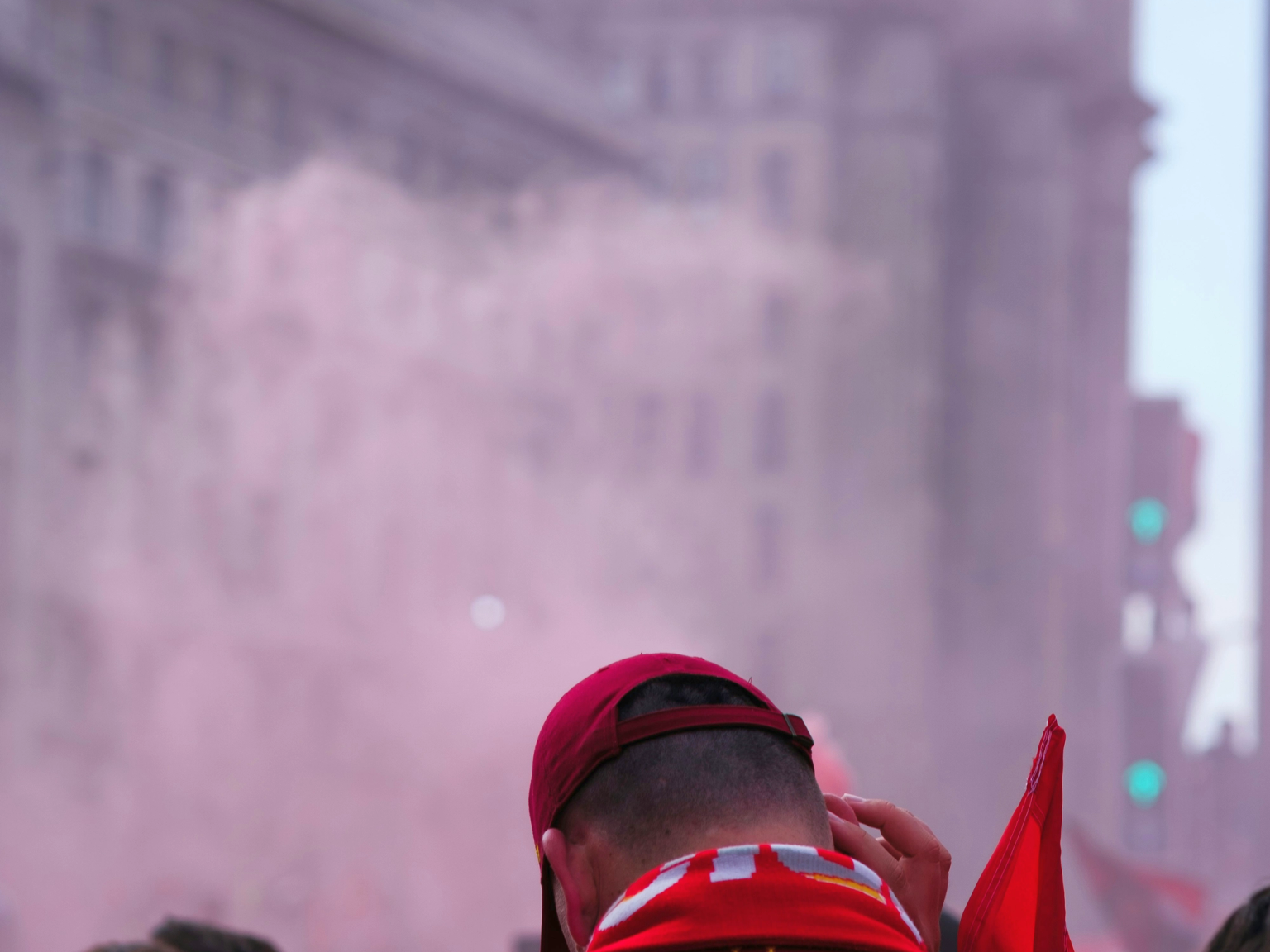 Fanin selkä punaisessa 'VIRGIL 4' pelipaidassa ja lippalakissa, vaaleanpunaisen savun ja sumeiden kaupunkirakennusten keskellä.