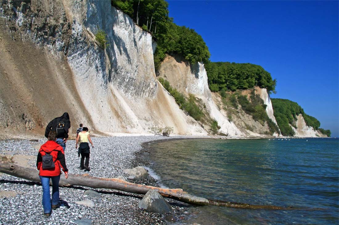 eine Gruppe von Menschen geht an einem felsigen Strand neben einem Gewässer entlang