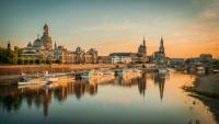 Dresdens Stadtsilhouette bei Sonnenaufgang, die historische Gebäude und Boote zeigt, die sich im ruhigen Elbe-Fluss spiegeln.